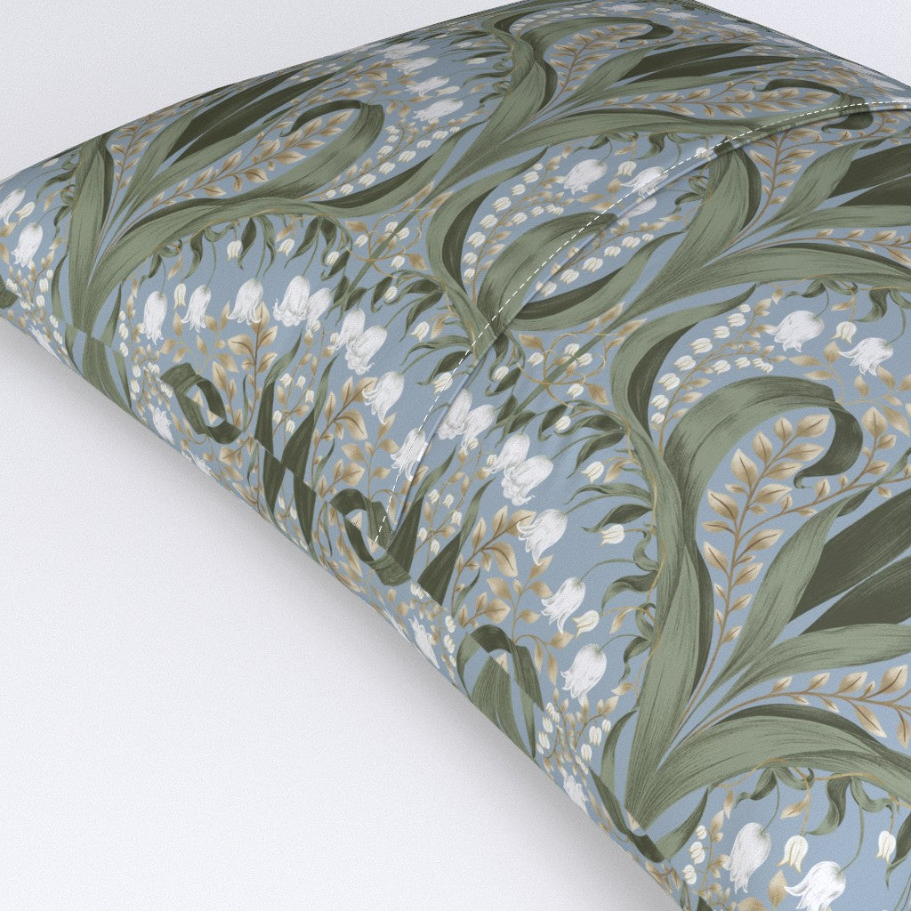 Decorative pillow with an Art Nouveau botanical pattern featuring green leaves and white lily‑of‑the‑valley flowers on a steel blue background.