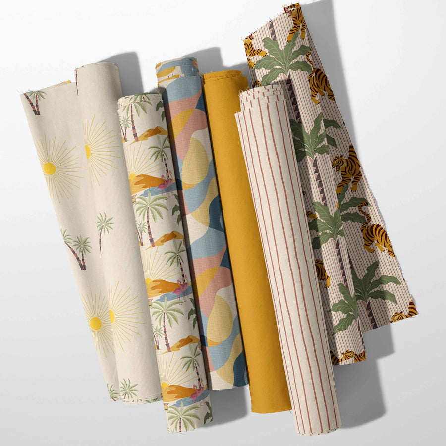 Retro Oasis surface pattern collection by Noemi Marozsan displayed on rolled fabric featuring tropical palm trees tiger stripe sun and desert landscape prints in ochre teal blush and cream