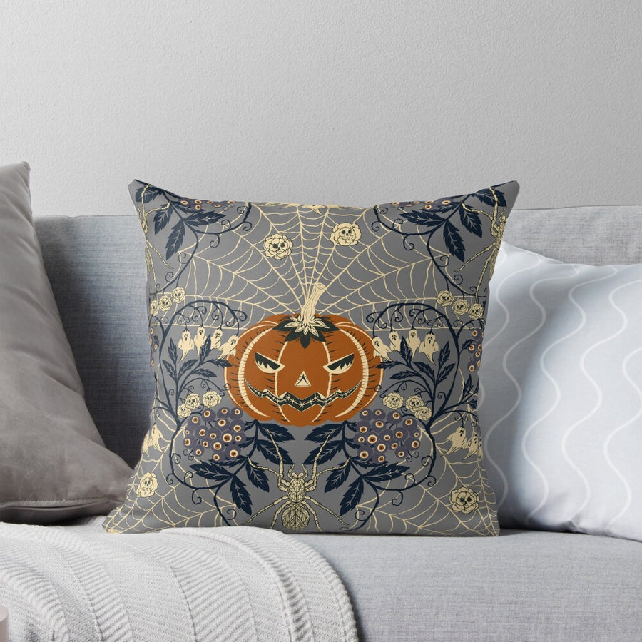 A Halloween pillow with a carved pumpkin in the center, surrounded by webs, skulls, spiders, and floral patterns
